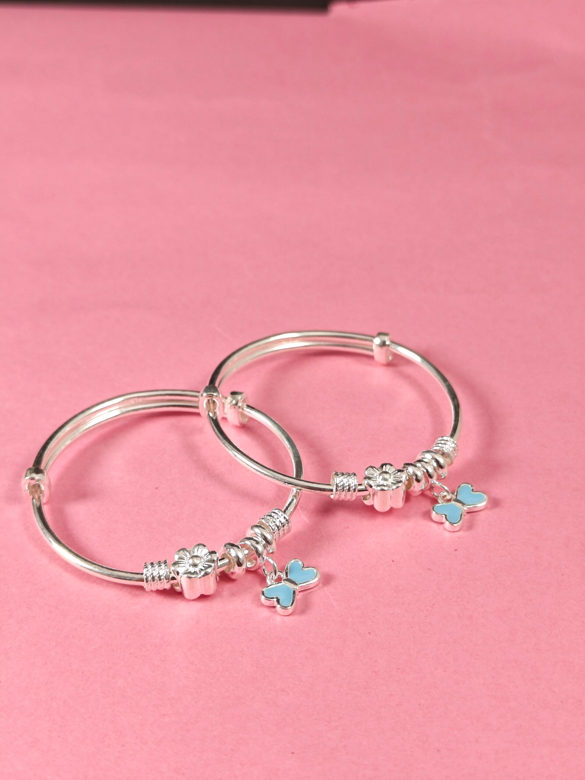 Silver bangle with butterfly charms on a pink background